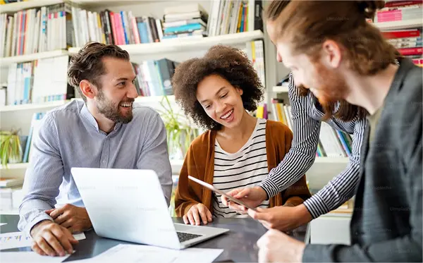 4 smiling people sit around a laptop